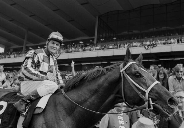 A jockey raises a finger in victory atop a champion thoroughbred — a Triple Crown moment.